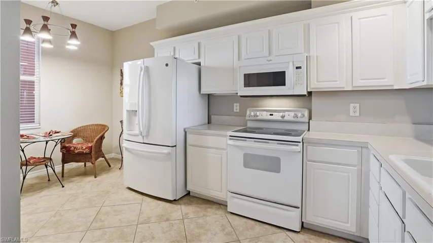 Kitchen featuring white appliances, light countertops, white cabinets, decorative light fixtures, and light tile patterned flooring - Virtually Edited Image