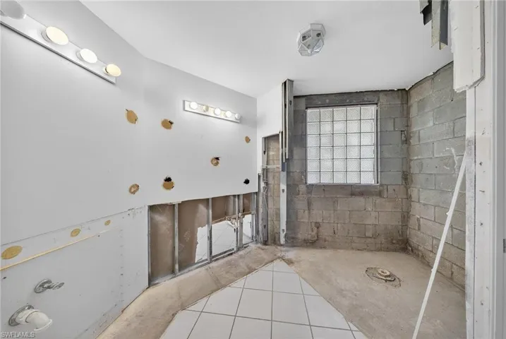Bathroom with tiled shower, concrete block wall, and light tile patterned floors