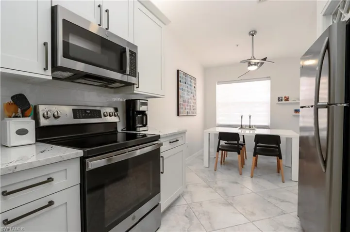 Kitchen with stainless steel appliances, light marble finish flooring, light stone countertops, and white cabinets