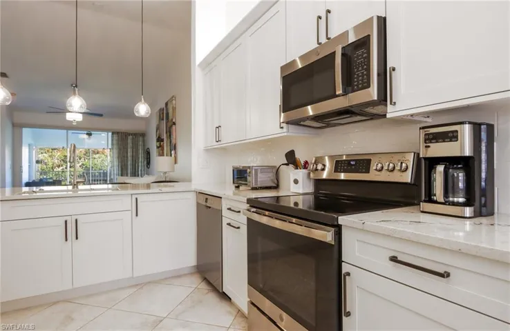 Kitchen with appliances with stainless steel finishes, light stone counters, white cabinets, light tile patterned floors, and decorative light fixtures