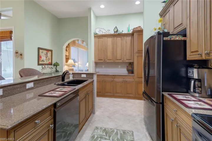 Kitchen featuring backsplash, sink, light stone counters, light tile patterned floors, and black appliances