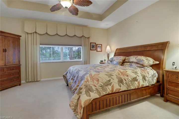 Bedroom with ceiling fan, a raised ceiling, and light colored carpet