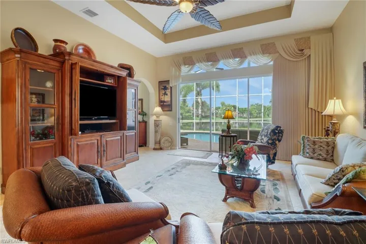 Living room with ceiling fan, a raised ceiling, and light tile patterned floors