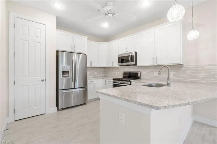 Kitchen featuring a sink, appliances with stainless steel finishes, a peninsula, white cabinets, and decorative backsplash