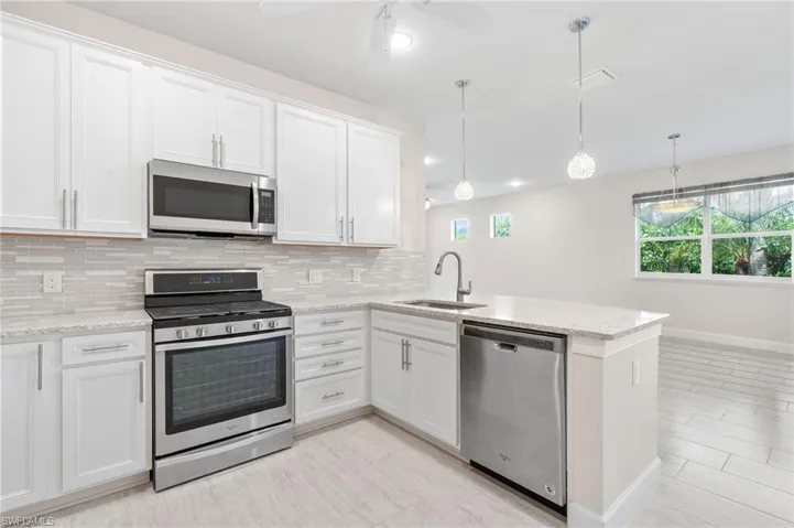 Kitchen featuring backsplash, a sink, white cabinets, a peninsula, and appliances with stainless steel finishes