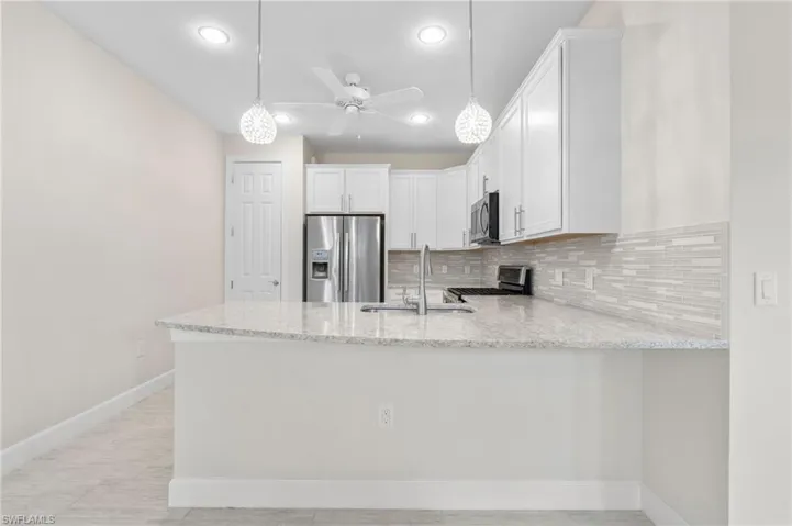 Kitchen featuring light stone counters, a peninsula, decorative backsplash, and stainless steel appliances