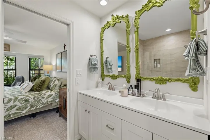 Ensuite bathroom featuring ensuite bath, tiled shower, double vanity, and a sink