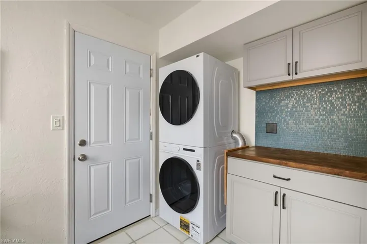 Laundry room with light tile patterned floors, stacked washer / drying machine, and cabinet space