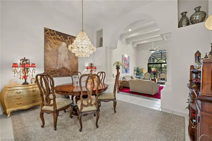 Tiled dining room with arched walkways, ceiling fan with notable chandelier, a high ceiling, and decorative columns