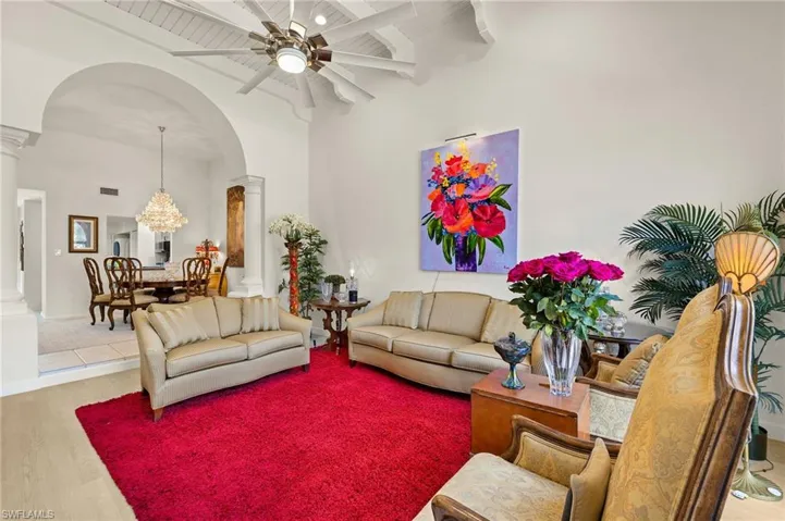 Living area with a ceiling fan, wood finished floors, arched walkways, decorative columns, and a towering ceiling