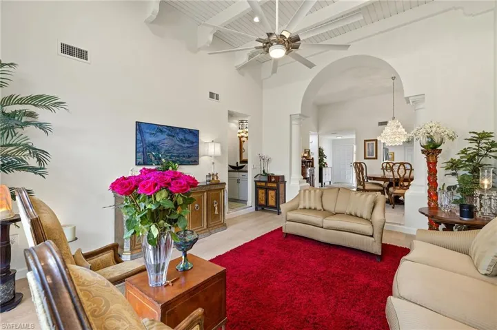 Living area with a ceiling fan, visible vents, beam ceiling, light wood-style flooring, and arched walkways