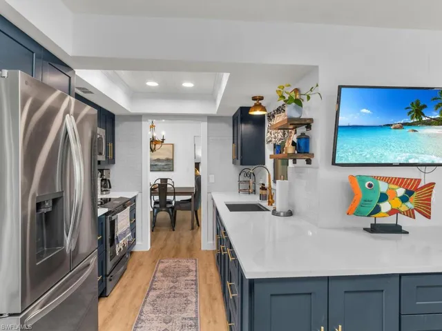 Kitchen featuring appliances with stainless steel finishes, a raised ceiling, sink, light hardwood / wood-style flooring, and an inviting chandelier