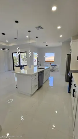Kitchen featuring white cabinetry, pendant lighting, recessed lighting, a large island with sink, and light stone countertops