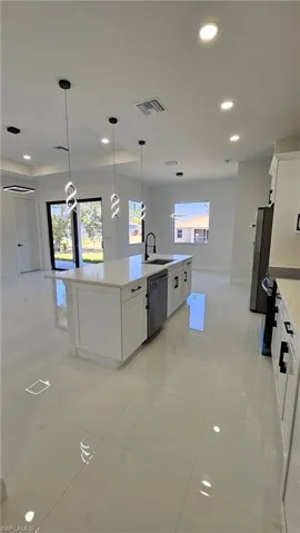 Kitchen featuring white cabinets, decorative light fixtures, recessed lighting, an island with sink, and stainless steel appliances