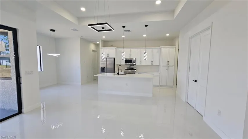 Kitchen with a tray ceiling, white cabinetry, a center island with sink, hanging light fixtures, and recessed lighting