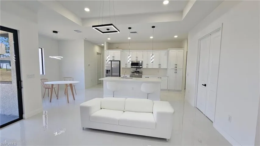 Kitchen featuring a tray ceiling, white cabinetry, an island with sink, appliances with stainless steel finishes, and recessed lighting