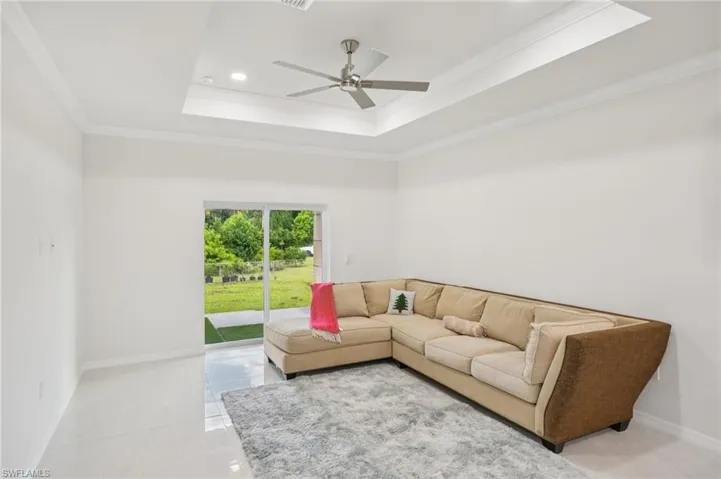 Living area with a raised ceiling, ornamental molding, light tile patterned flooring, a ceiling fan, and recessed lighting