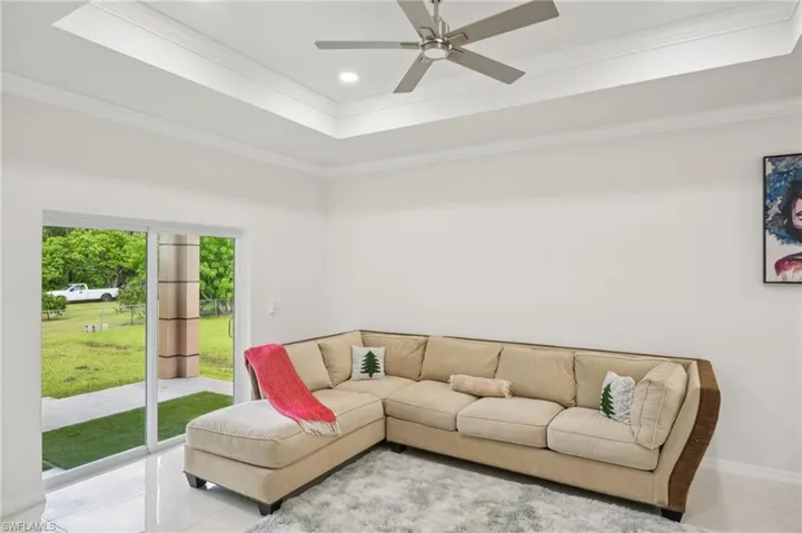 Living room featuring a raised ceiling, ornamental molding, recessed lighting, tile patterned flooring, and ceiling fan