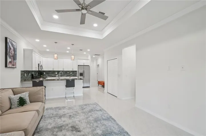 Living area with a tray ceiling, recessed lighting, ornamental molding, light tile patterned floors, and ceiling fan