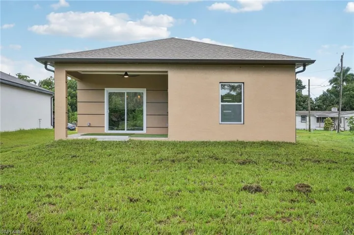 Back of house featuring a patio, a lawn, a ceiling fan, roof with shingles, and stucco siding