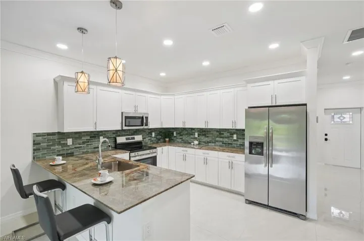 Kitchen with stainless steel appliances, dark stone countertops, white cabinetry, a breakfast bar, and ornamental molding