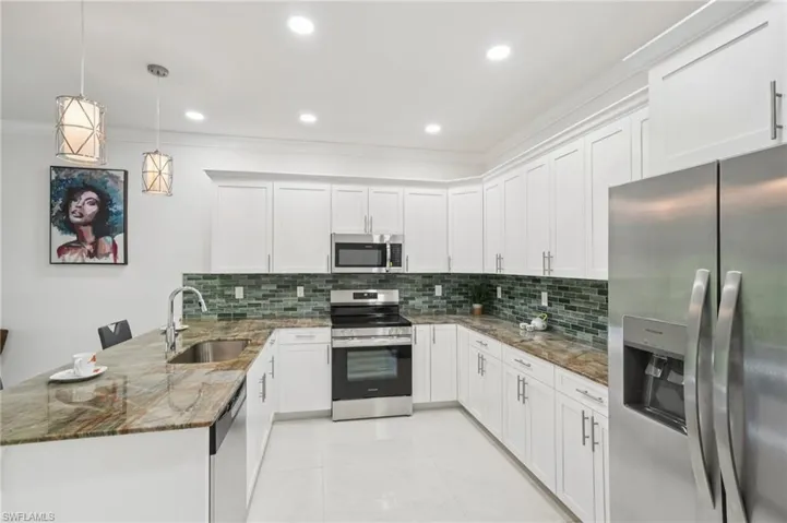 Kitchen featuring a peninsula, stainless steel appliances, dark stone counters, white cabinetry, and hanging light fixtures