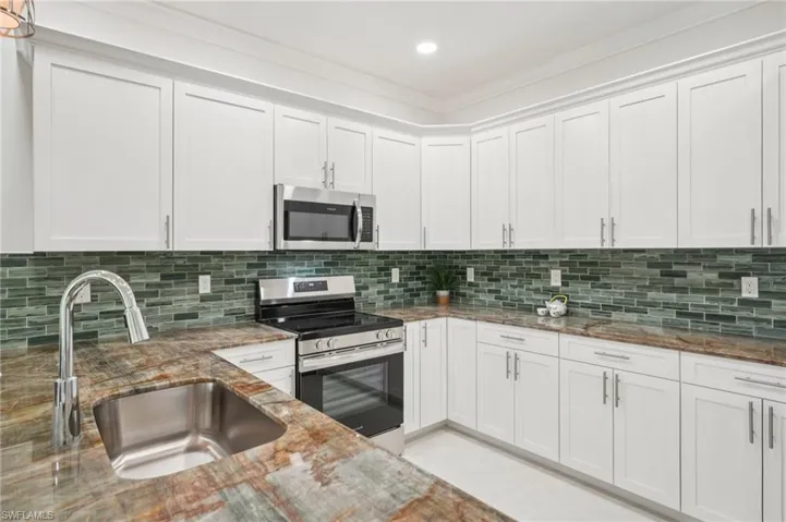 Kitchen featuring stainless steel appliances, white cabinets, decorative backsplash, light stone countertops, and ornamental molding