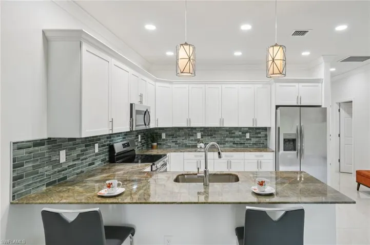 Kitchen with tasteful backsplash, dark stone countertops, crown molding, stainless steel appliances, and white cabinetry