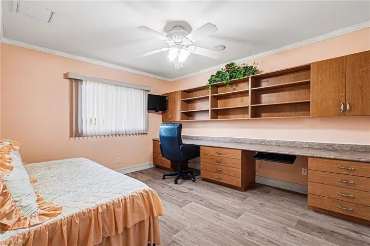Bedroom featuring light wood finished floors, a ceiling fan, crown molding, and 2 persson built in desks
