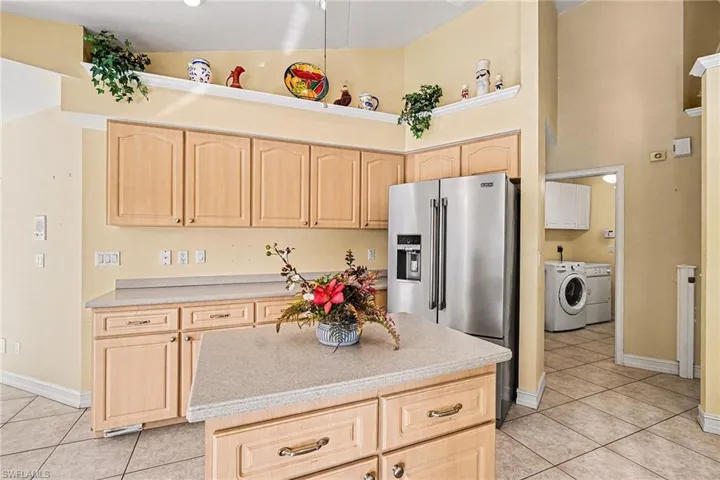 Kitchen with light brown cabinetry, high quality fridge, light tile patterned flooring, and a towering ceiling