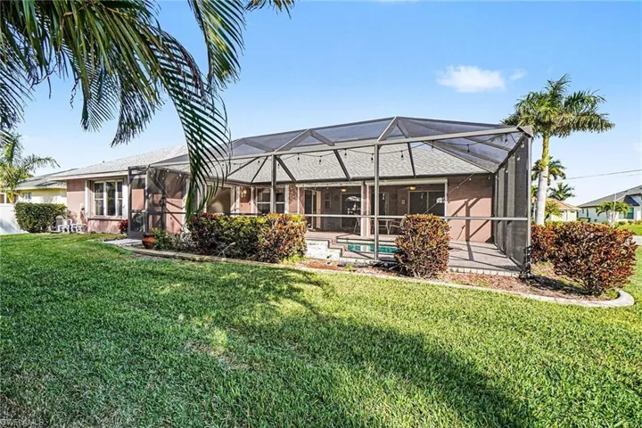 Back of house featuring screened enclosure, a lush lawn, and an outdoor pool