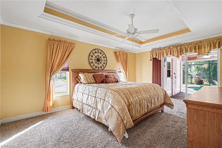 Carpeted bedroom with tray ceiling, crown molding with lighting, access to lanai, and a ceiling fan