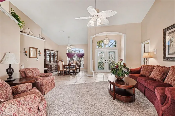 Living room featuring view of foyer double entry doors, high vaulted ceiling, ceiling fan, light tile patterned floors, and arched walkways