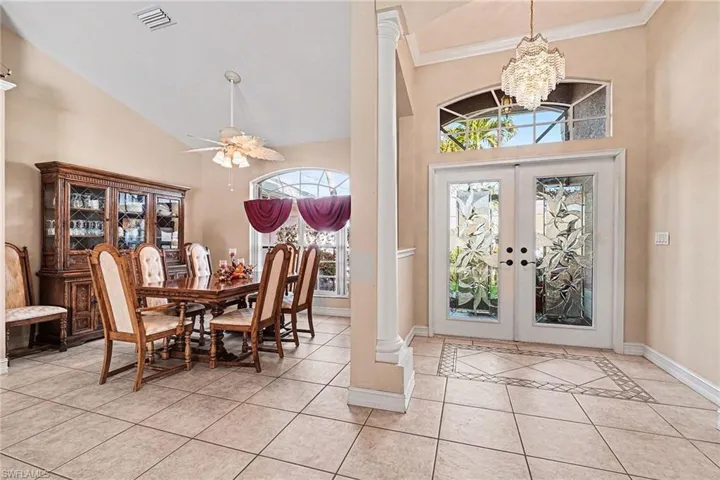 Entrance foyer with double entry glass doors, light tile patterned flooring, a towering ceiling, and a chandelier
