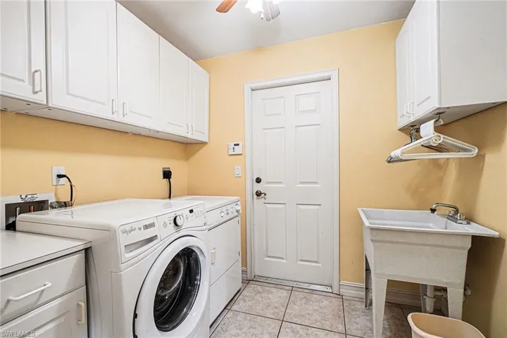Laundry room featuring cabinet space, light tile patterned floors, ceiling fan, and washing machine and dryer