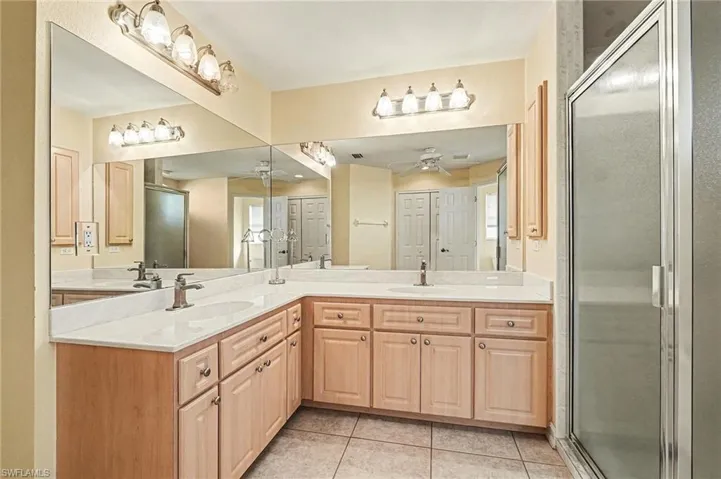 Full bath with double vanity, a shower stall, and light tile patterned flooring