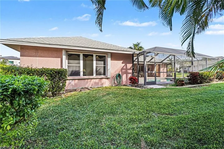 Rear view of property with stucco siding, glass enclosure, a lush lawn, and a shingled roof