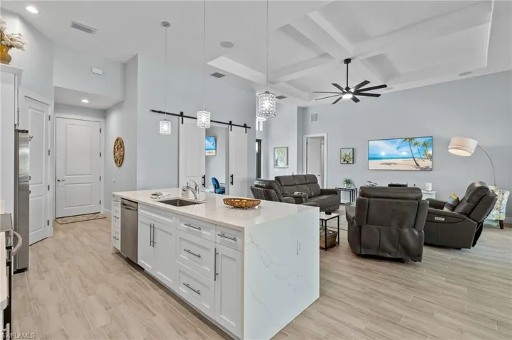 Kitchen with white cabinetry, an island with sink, a barn door to den, and coffered ceiling