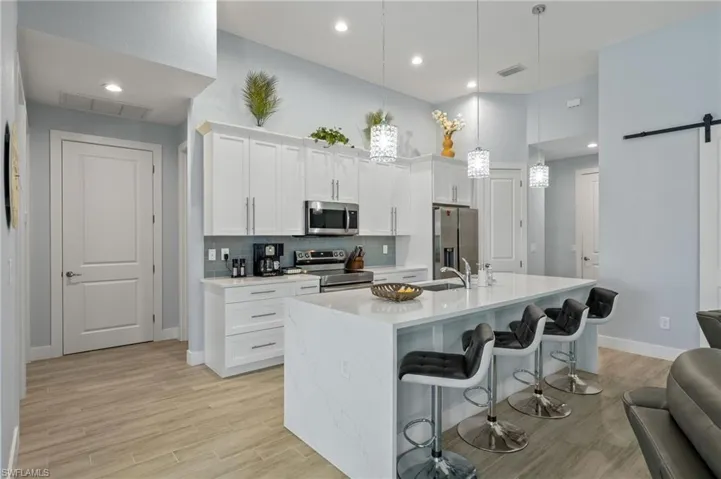 Kitchen featuring backsplash, appliances with stainless steel finishes, white cabinetry, and a barn door to the den