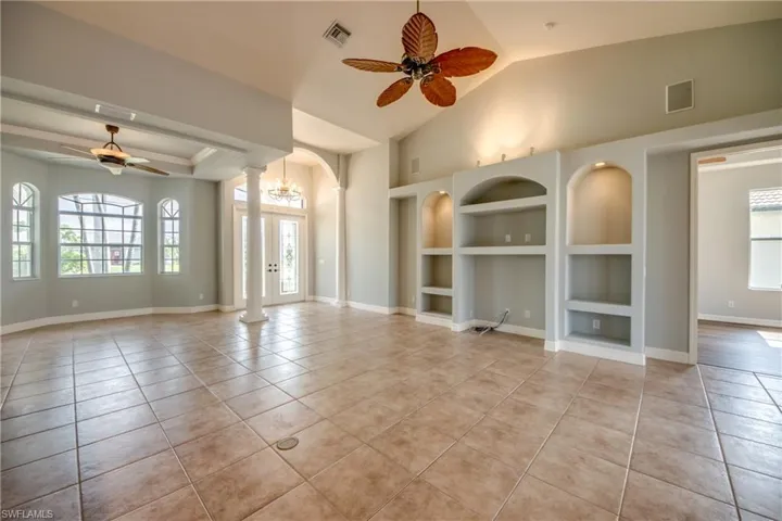 Unfurnished living room with ornate columns, light tile patterned floors, a wealth of natural light, and ceiling fan