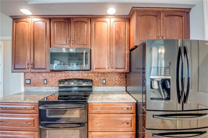 Kitchen with decorative backsplash, light stone counters, stainless steel appliances, and tile patterned floors