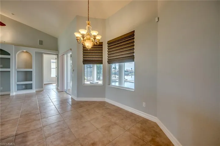 Unfurnished room featuring built in features, light tile patterned flooring, a notable chandelier, and a towering ceiling