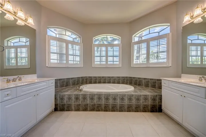 Bathroom with tiled tub, tile patterned flooring, and double vanity