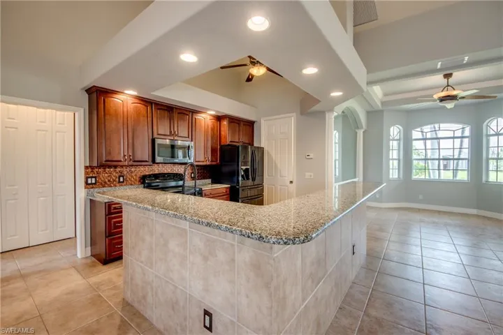 Kitchen featuring decorative backsplash, light stone countertops, black fridge with ice dispenser, and ceiling fan