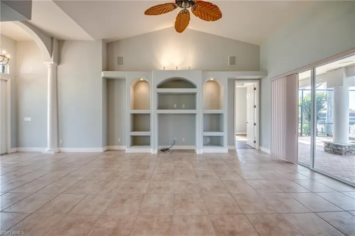 Unfurnished living room with built in shelves, ornate columns, light tile patterned floors, and ceiling fan
