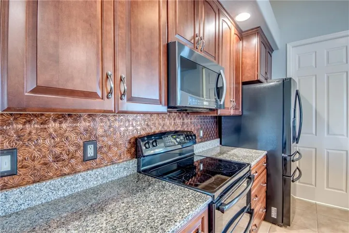 Kitchen featuring appliances with stainless steel finishes, dark stone countertops, light tile patterned floors, and decorative backsplash