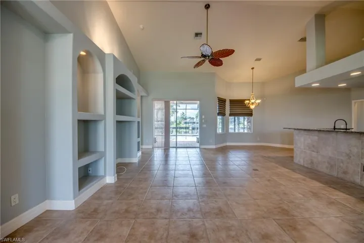 Unfurnished living room with built in features, sink, a high ceiling, ceiling fan with notable chandelier, and light tile patterned flooring