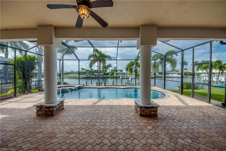 View of pool with a lanai, a water view, a patio, and ceiling fan