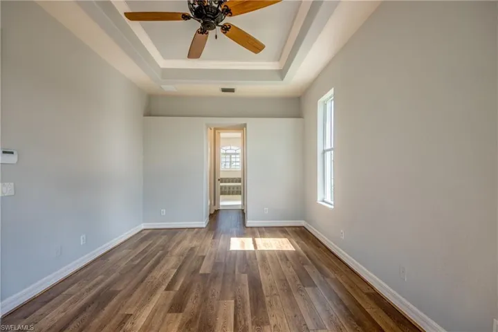 Empty room featuring ceiling fan, wood-type flooring, and a raised ceiling