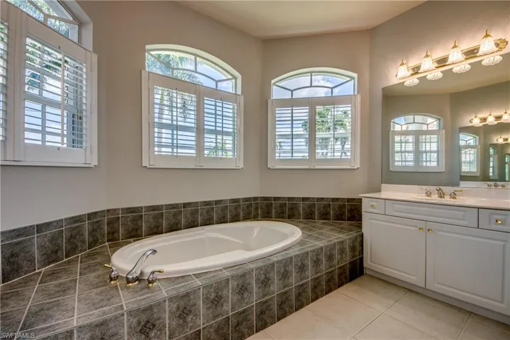 Bathroom featuring a relaxing tiled tub, tile patterned floors, and vanity